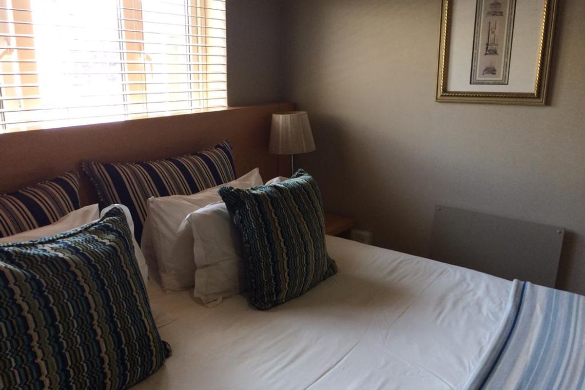 A cozy bedroom featuring a built-in headboard, venetian blinds for light control, and a wall-mounted panel heater for comfort.