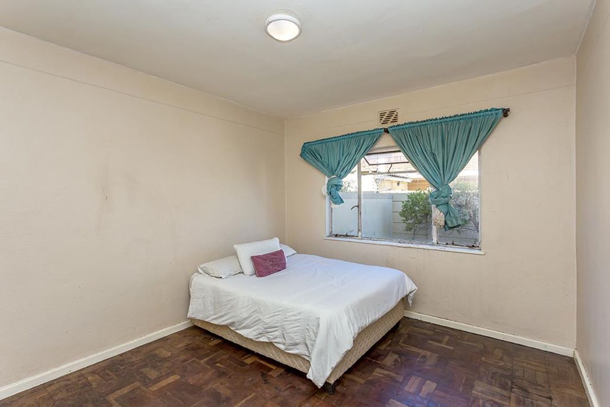 A bedroom featuring original parquet flooring and a steel-framed window, requiring cosmetic updates to the walls and flooring to improve its overall condition.
