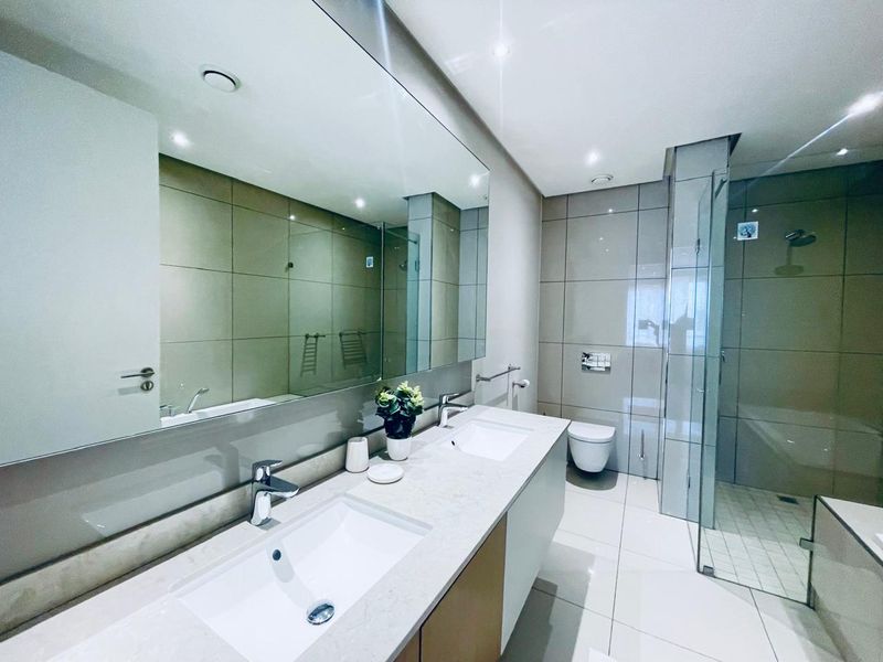Modern bathroom featuring a double vanity, wall-mounted toilet, and a spacious walk-in shower with contemporary tiling and large mirror.