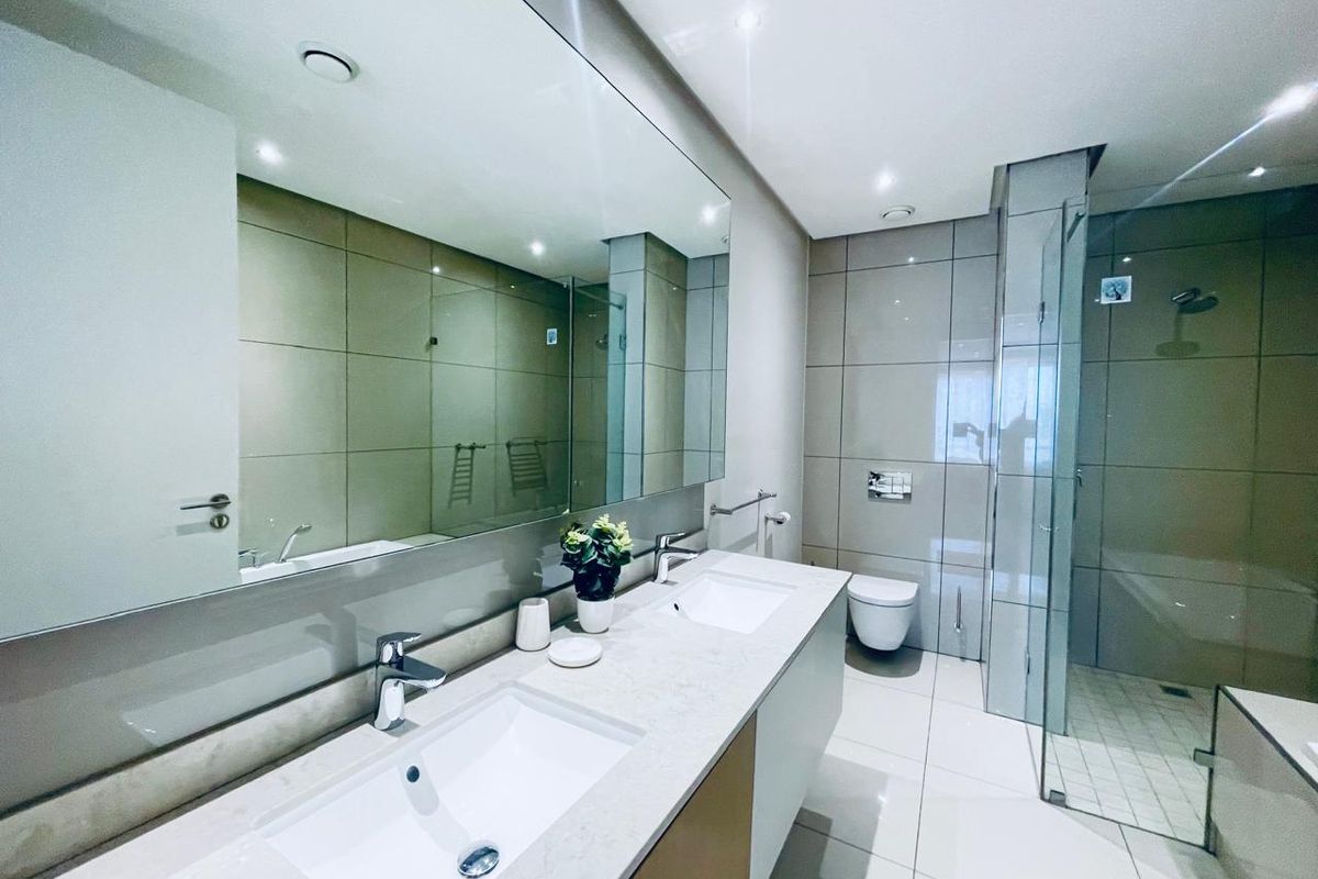 Modern bathroom featuring a double vanity, wall-mounted toilet, and a spacious walk-in shower with contemporary tiling and large mirror.