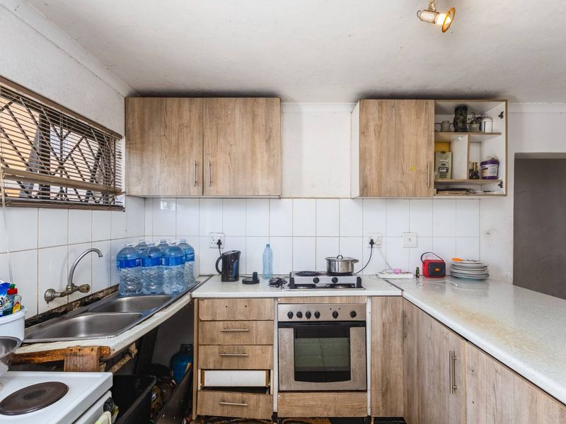 A functional kitchen featuring wood-look cabinetry, a built-in oven and hob, tiled backsplash, and double sink, requiring cosmetic updates to improve its overall condition.