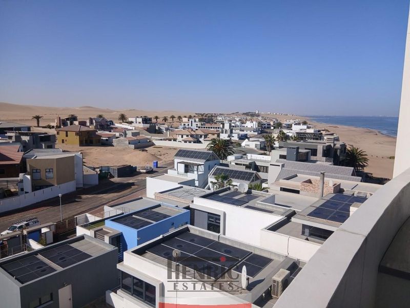 Elevated coastal view overlooking a residential neighborhood with solar panel installations and the ocean in the distance.