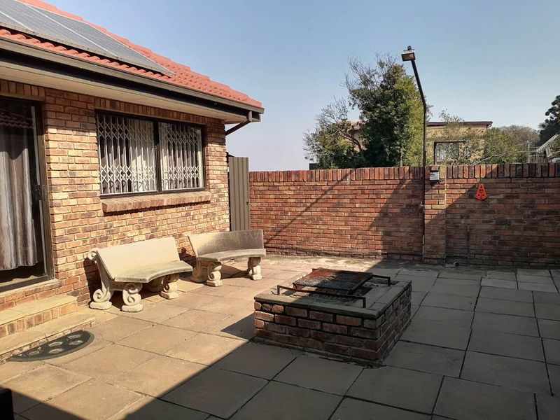 A paved outdoor patio area featuring a built-in brick braai, enclosed by a brick boundary wall and attached to the main house structure.