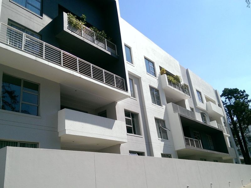 A modern apartment building exterior featuring clean architectural lines, private balconies with metal railings, and a well-maintained concrete facade.