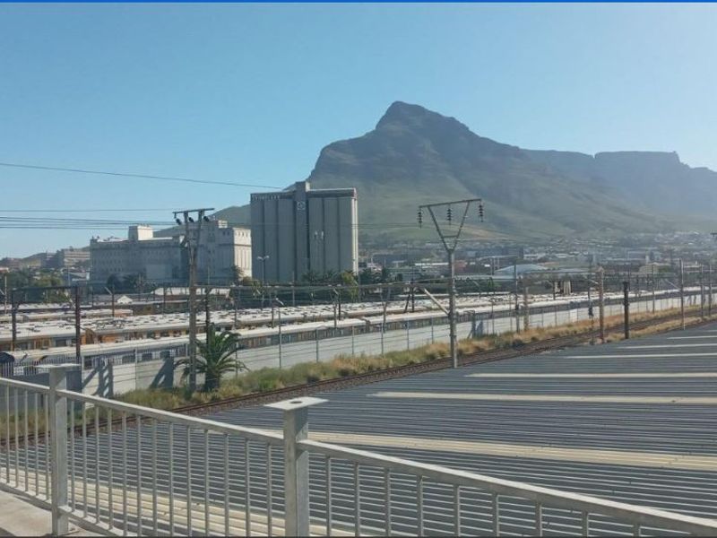 An elevated view overlooking a railway yard with industrial buildings and a prominent mountain range in the background.