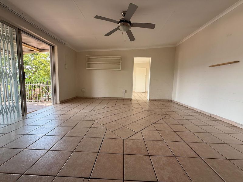 An empty, open-plan living area featuring neutral tiled flooring, a ceiling fan, and direct access to an outdoor patio through sliding glass doors.