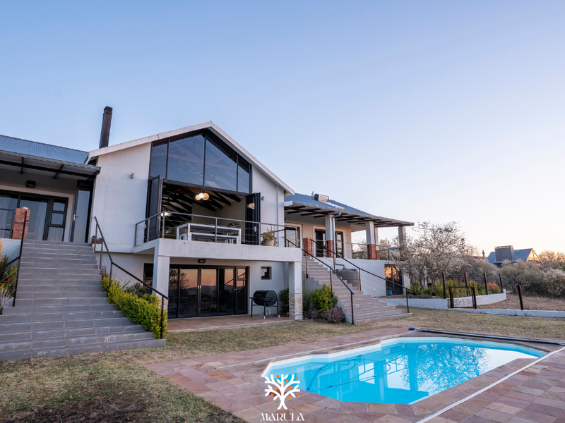 Rear view of a modern house featuring a raised patio, bi-fold doors, metal staircases, and a swimming pool with stone paving.