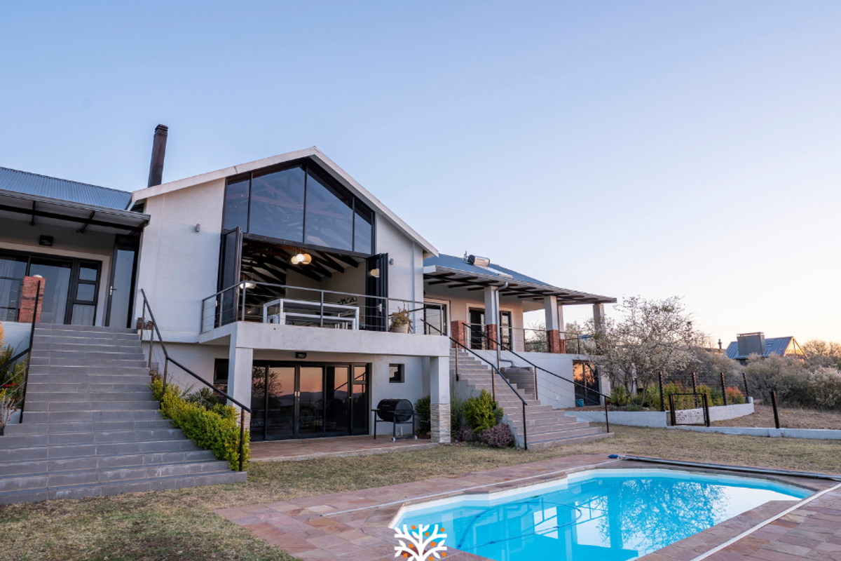 Rear view of a modern house featuring a raised patio, bi-fold doors, metal staircases, and a swimming pool with stone paving.