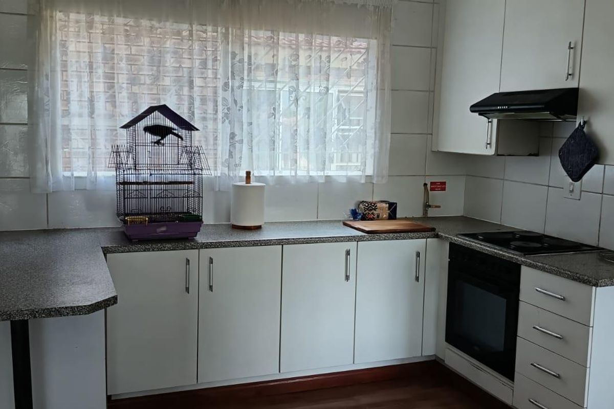A functional kitchen featuring white cabinetry, granite-look laminate countertops, a built-in oven, and an electric hob with an extractor fan.