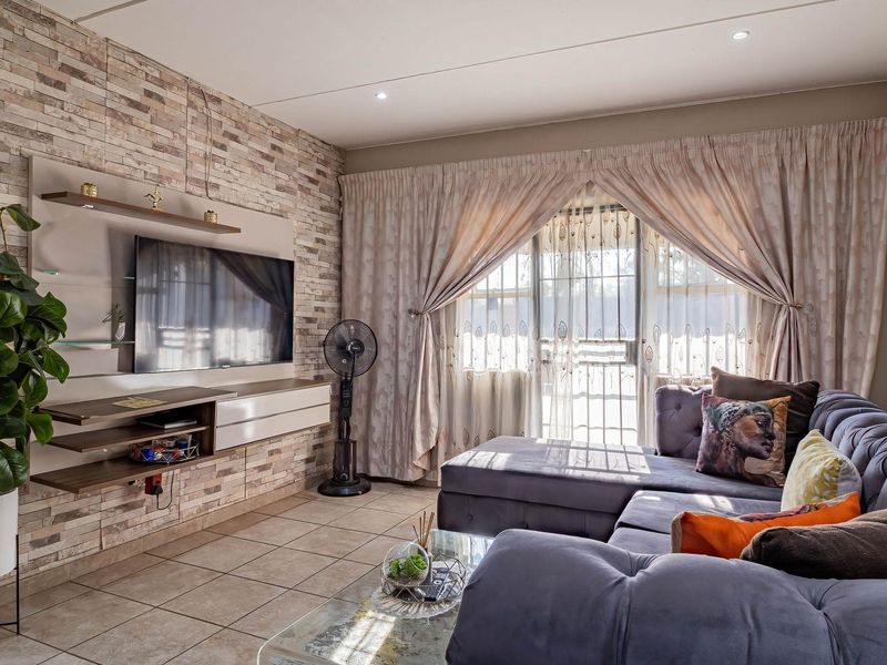 A well-maintained living room featuring a textured stone veneer accent wall, built-in media cabinetry, tiled flooring, and large sliding doors leading to an outdoor area.