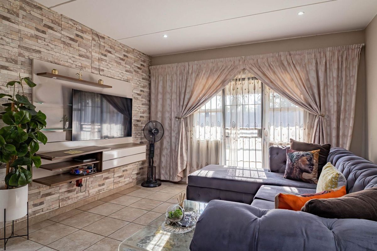 A well-maintained living room featuring a textured stone veneer accent wall, built-in media cabinetry, tiled flooring, and large sliding doors leading to an outdoor area.