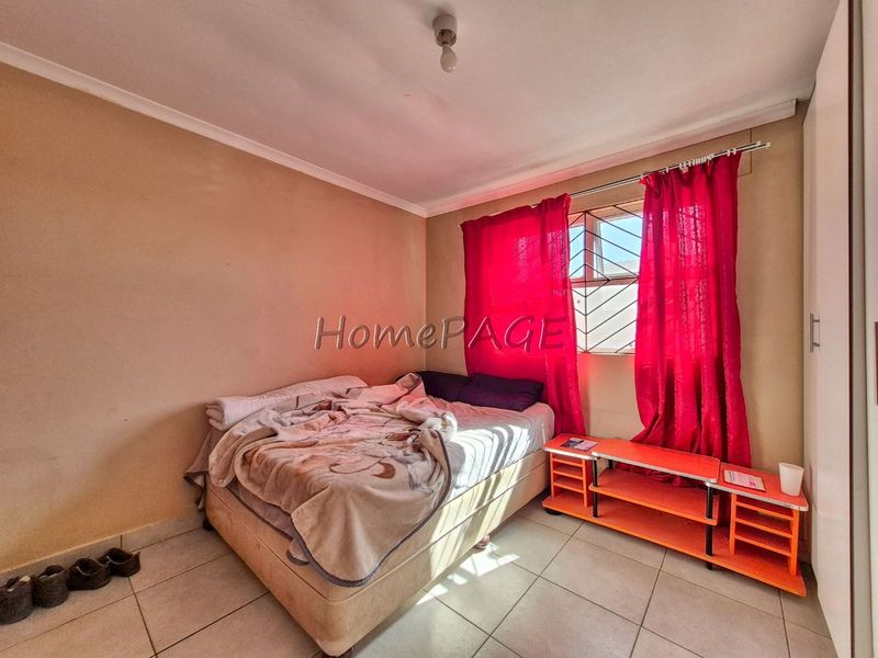 A bedroom featuring tiled flooring, built-in wardrobe, and security bars on the window. The room requires cosmetic updates to improve its overall condition.