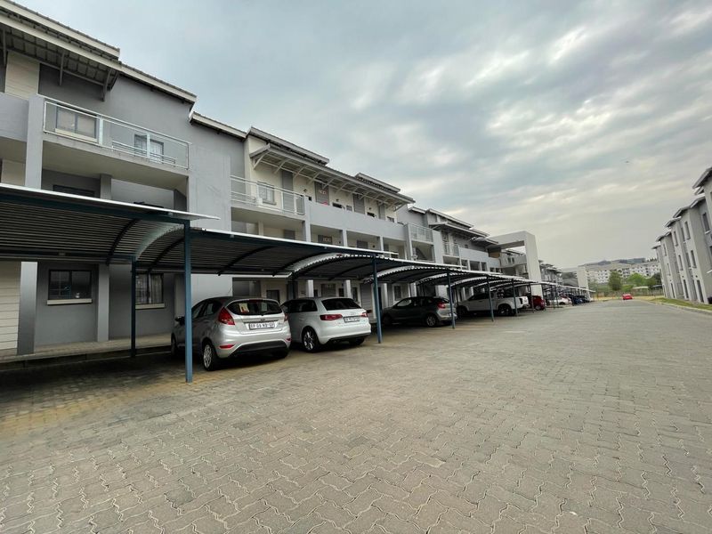 Exterior view of a modern apartment complex featuring covered parking bays and paved driveway access.