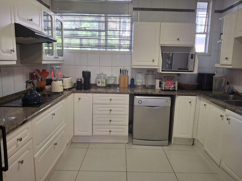 A functional kitchen featuring white cabinetry, granite countertops, ceramic tile flooring, and integrated appliances including a dishwasher and built-in microwave.