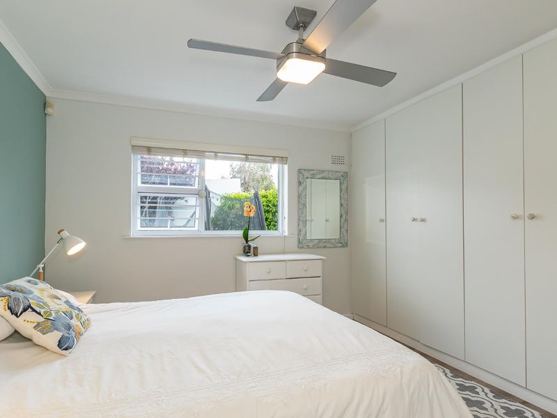 A well-maintained bedroom featuring built-in cupboards, a modern ceiling fan, and a window providing natural light.