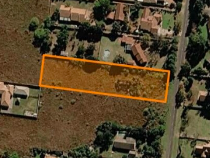 Aerial view of a vacant residential plot highlighted in an orange boundary, situated within an established suburban neighborhood.