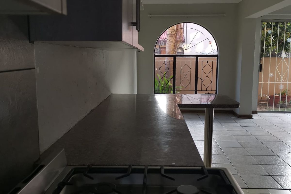 A functional kitchen area featuring a gas hob, granite countertops, and tiled flooring, leading out to a patio through a secure arched window and door.