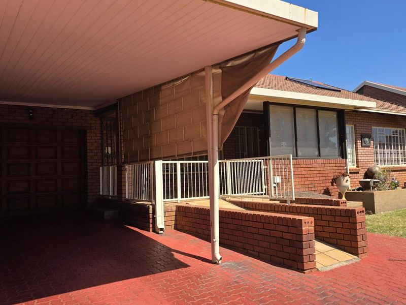 Front exterior view featuring a brick facade, paved driveway, carport, and a brick ramp with metal railing leading to the entrance.