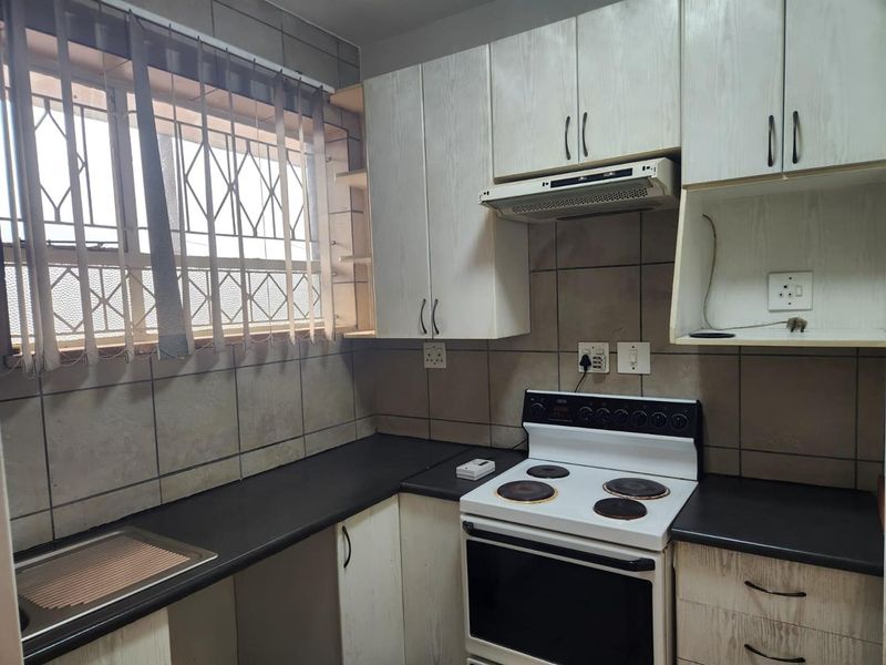 A functional kitchen featuring built-in cabinetry, laminate countertops, a tiled backsplash, and a freestanding electric stove with an integrated extractor fan.
