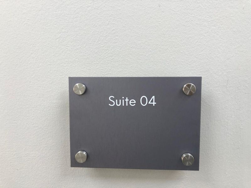 A close-up view of a modern grey office suite identification sign mounted on a wall.