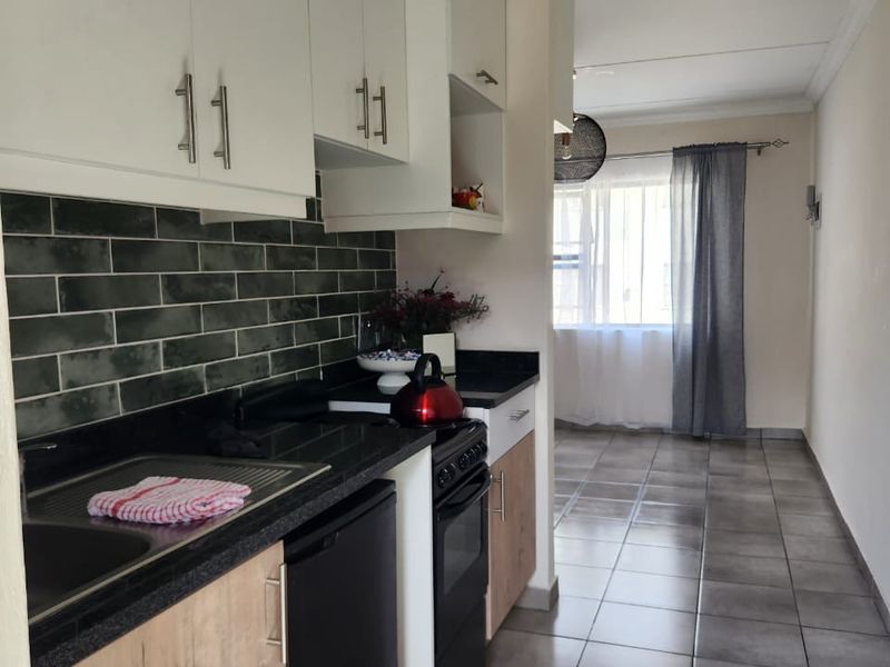 A modern kitchen featuring white and wood-tone cabinetry, dark stone countertops, a green subway tile backsplash, and neutral floor tiles.