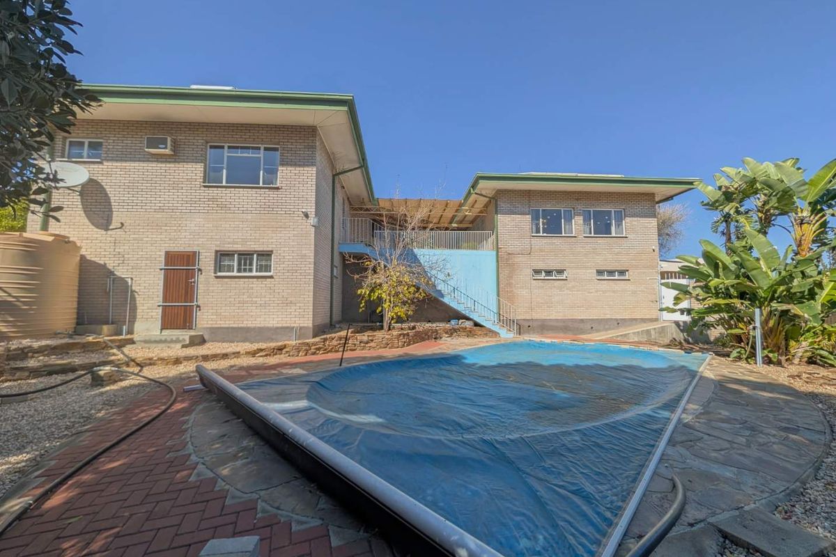 Rear view of a brick house featuring a swimming pool with a cover, paved patio area, and an external staircase leading to the upper level.