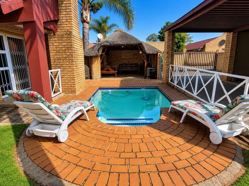 Outdoor entertainment area featuring a swimming pool, brick-paved surround, and a traditional thatched lapa, perfect for relaxation and hosting guests.
