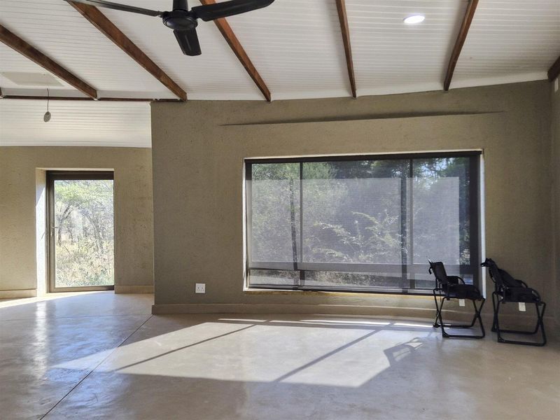 Spacious living area featuring polished concrete floors, exposed timber ceiling beams, and large windows providing natural light and garden views.