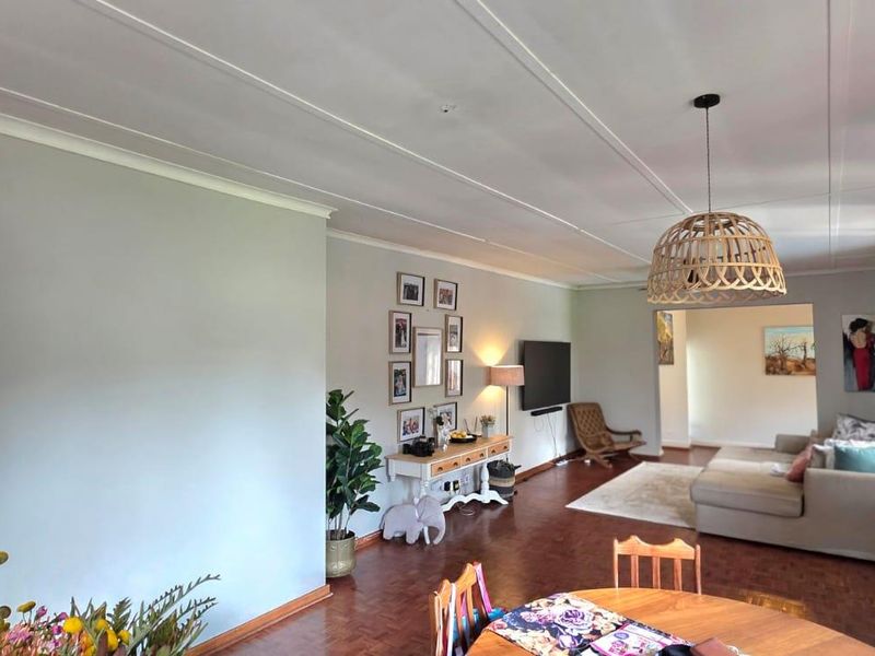Spacious open-plan living and dining area featuring warm parquet flooring, coved ceilings, and a central pendant light fixture.