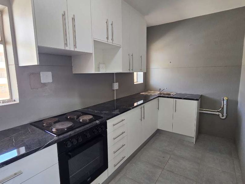 A clean, modern kitchen featuring white cabinetry, black stone countertops, a built-in oven and hob, and neutral floor tiles.