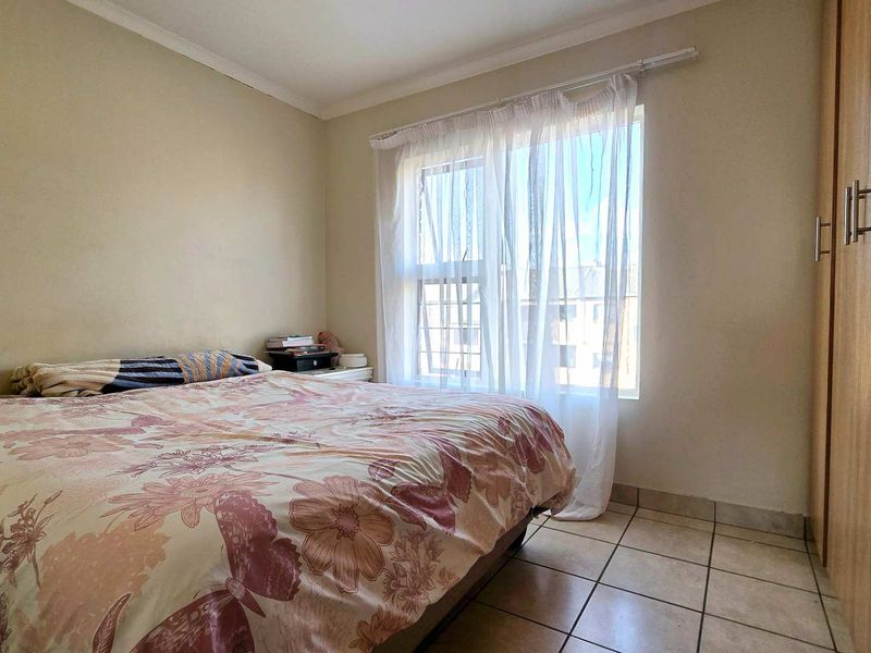 A functional bedroom featuring tiled flooring, a built-in wardrobe, and natural light from a window.
