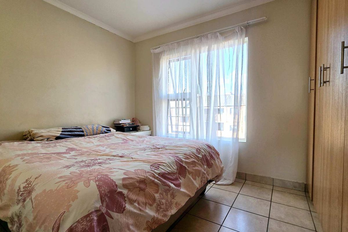 A functional bedroom featuring tiled flooring, a built-in wardrobe, and natural light from a window.