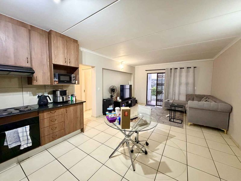 Open-plan living area featuring a functional kitchen with built-in cabinetry, electric hob, and oven, flowing into a lounge space with access to a balcony.