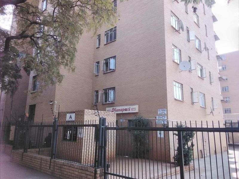 Exterior view of the Monopati apartment building featuring a brick facade, secure perimeter fencing, and gated entrance.