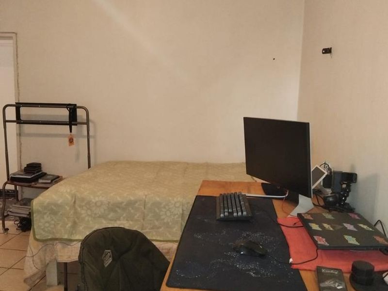 A bedroom featuring tiled flooring and a ceiling fan, currently utilized as a combined sleeping and workspace area.