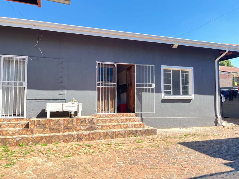 Rear exterior view of the house featuring a paved area, tiled entrance steps, and security gates on doors and windows.