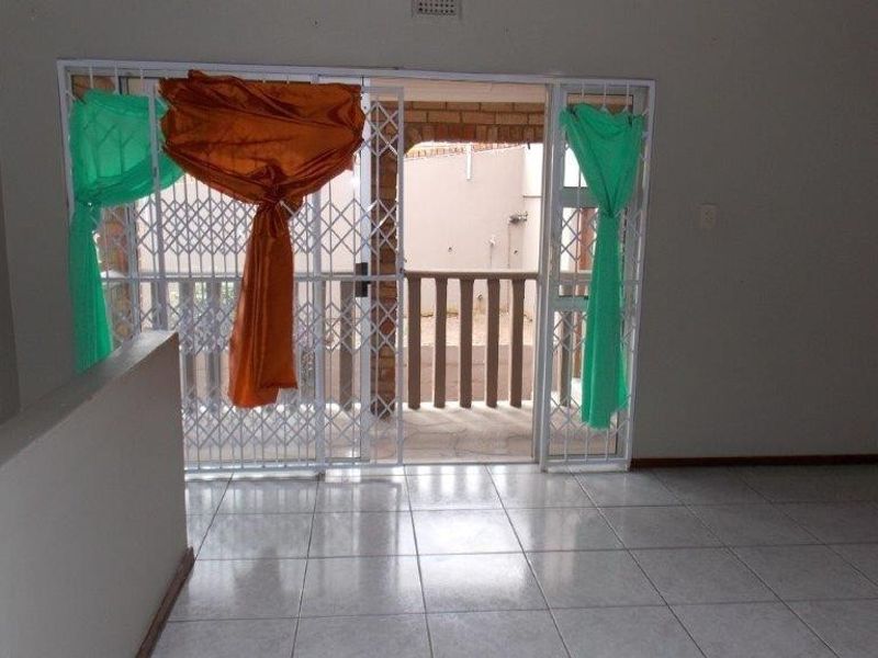 An empty living area featuring tiled flooring and a sliding door with a security gate leading out to a balcony.