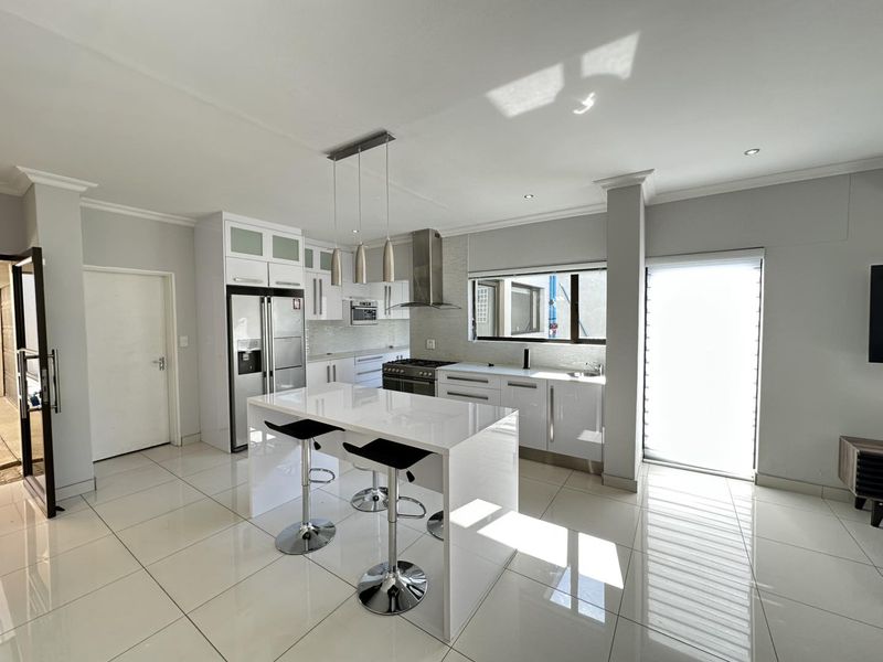 Modern kitchen featuring high-gloss cabinetry, a central island with breakfast bar, stainless steel appliances, and polished floor tiles.