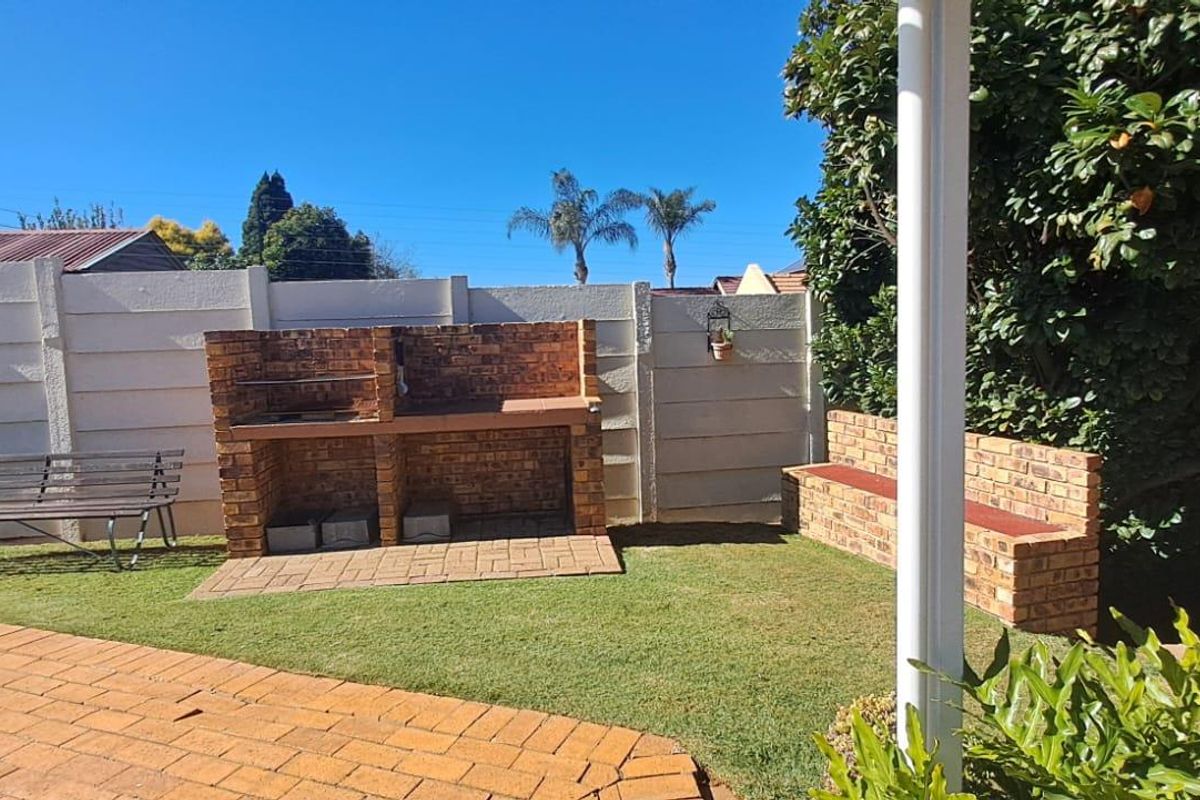A private rear garden featuring a built-in brick braai area, paved patio section, and perimeter walling.
