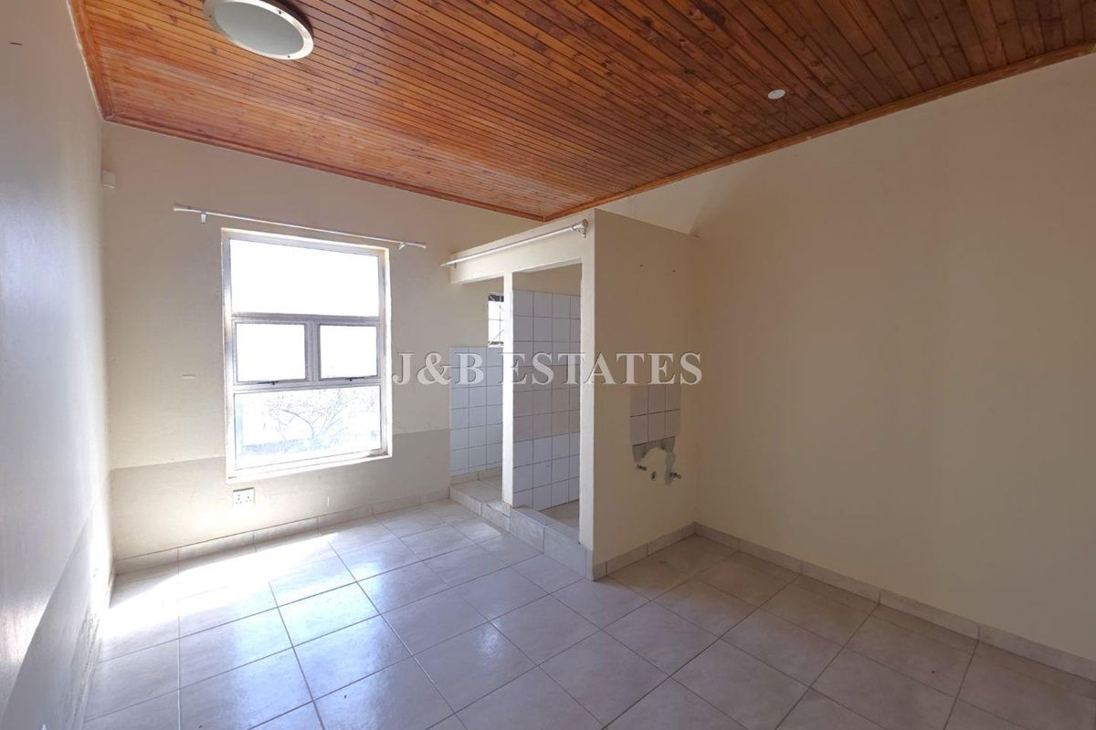 An empty bedroom featuring a timber-clad ceiling, tiled flooring, and an integrated en-suite bathroom area with exposed plumbing fixtures.