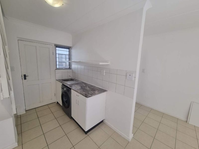 A functional laundry area featuring tiled flooring, built-in cabinetry with a laminate countertop, a stainless steel sink, and a tiled splashback.