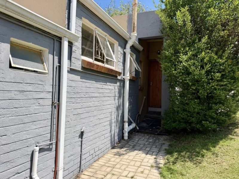 Rear exterior view of the apartment featuring a painted brick facade, paved walkway, and functional casement windows with security bars.