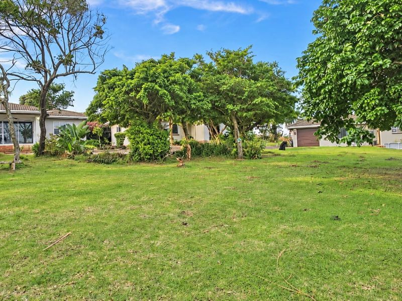 A spacious, well-maintained garden area featuring mature trees and lawn, providing a view of the property's rear exterior and garage structure.