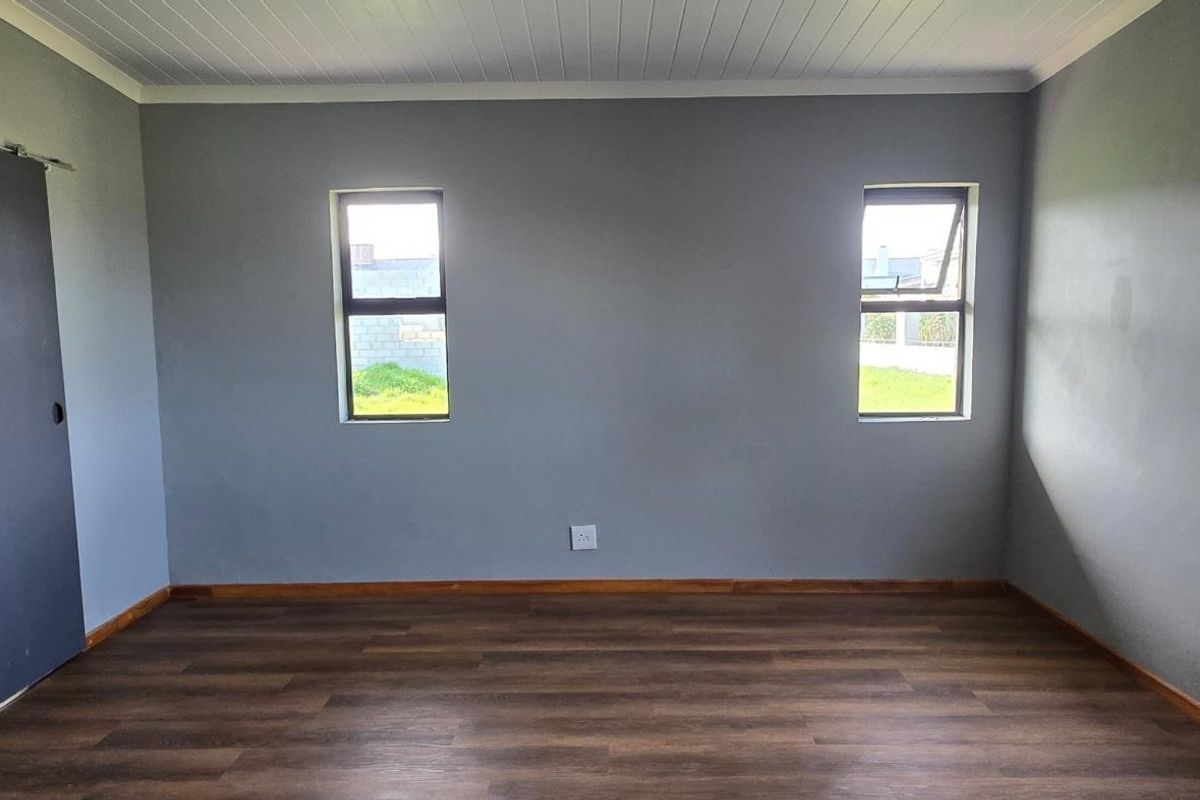 A bright, empty bedroom featuring modern wood-look laminate flooring, grey painted walls, and a sliding barn-style door.