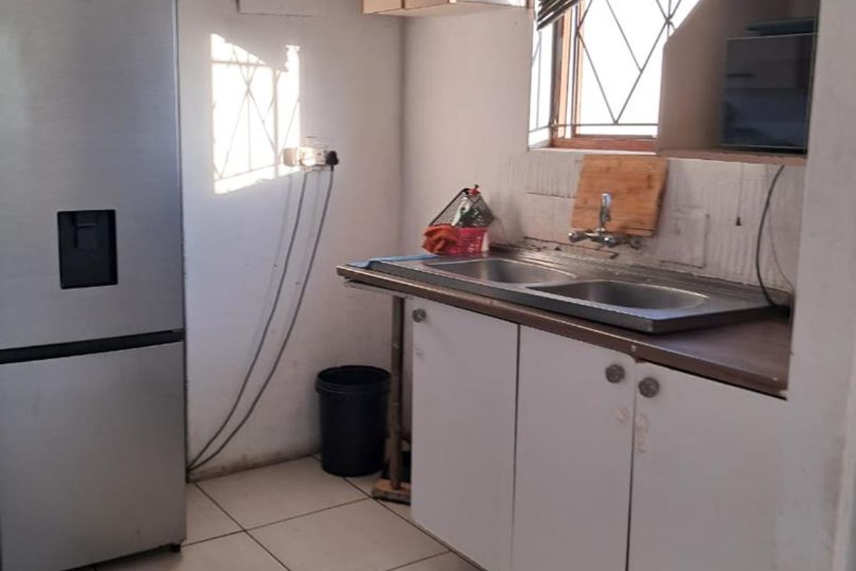 A compact kitchen featuring tiled flooring, built-in cabinetry, and a double sink, requiring cosmetic updates to improve functionality and aesthetic appeal.