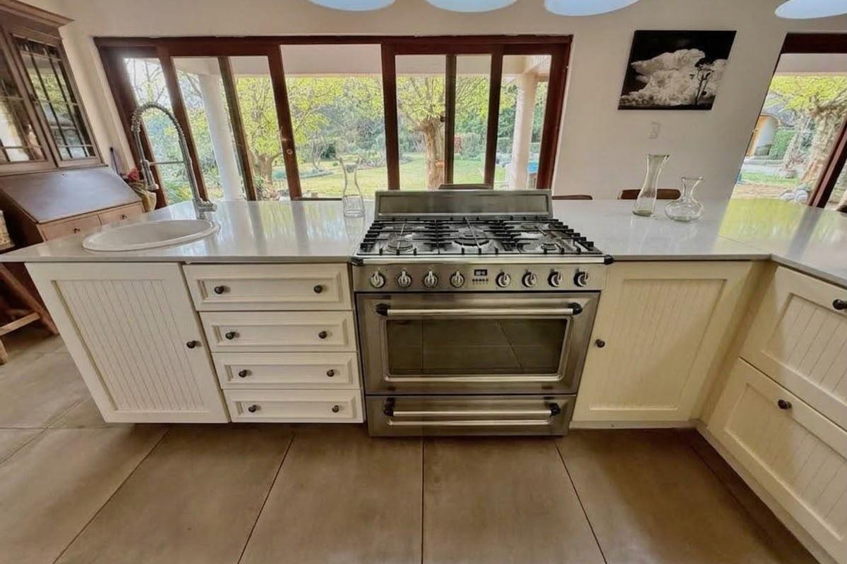 A well-appointed kitchen featuring a stainless steel gas stove, stone countertops, an undermount sink, and large sliding doors overlooking the garden.