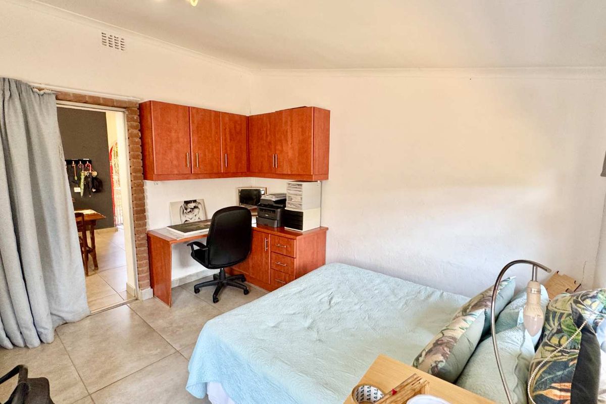 A functional bedroom featuring built-in wooden cabinetry and desk space, tiled flooring, and direct access to an adjacent room.