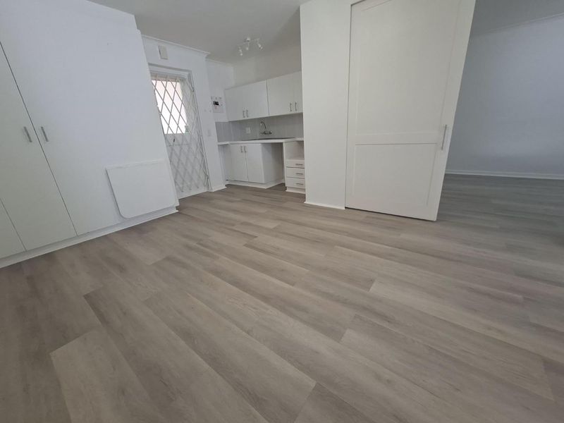 An open-plan living area featuring modern laminate flooring, built-in cabinetry, and a functional kitchenette with a sink and tiled backsplash.