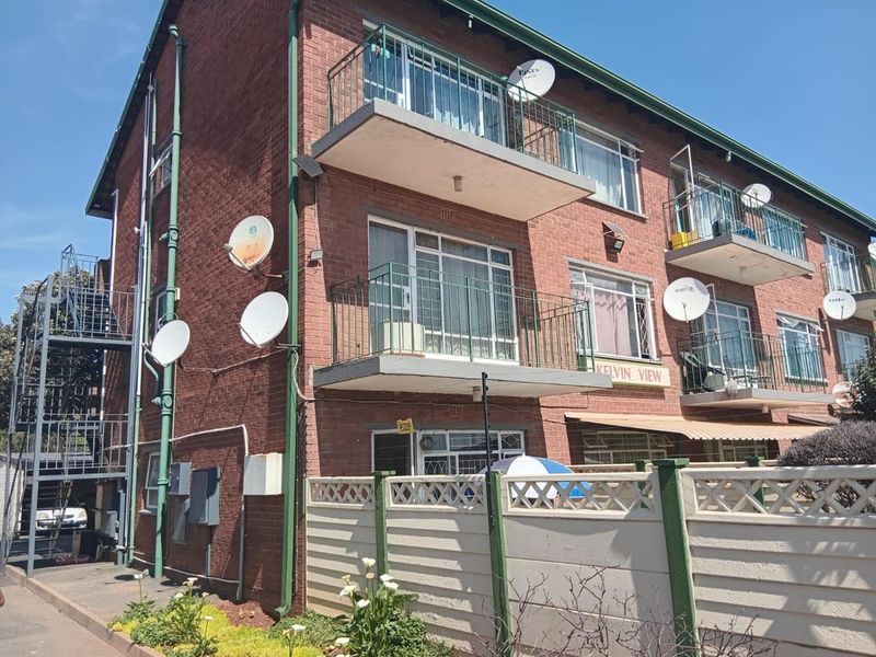 Exterior view of a multi-story brick apartment building featuring private balconies, metal railings, and an external staircase.