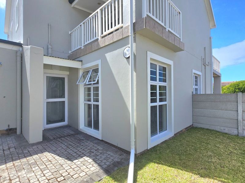 Rear exterior view of the house featuring a paved patio area, a balcony with white railings, and a small private garden with boundary walling.